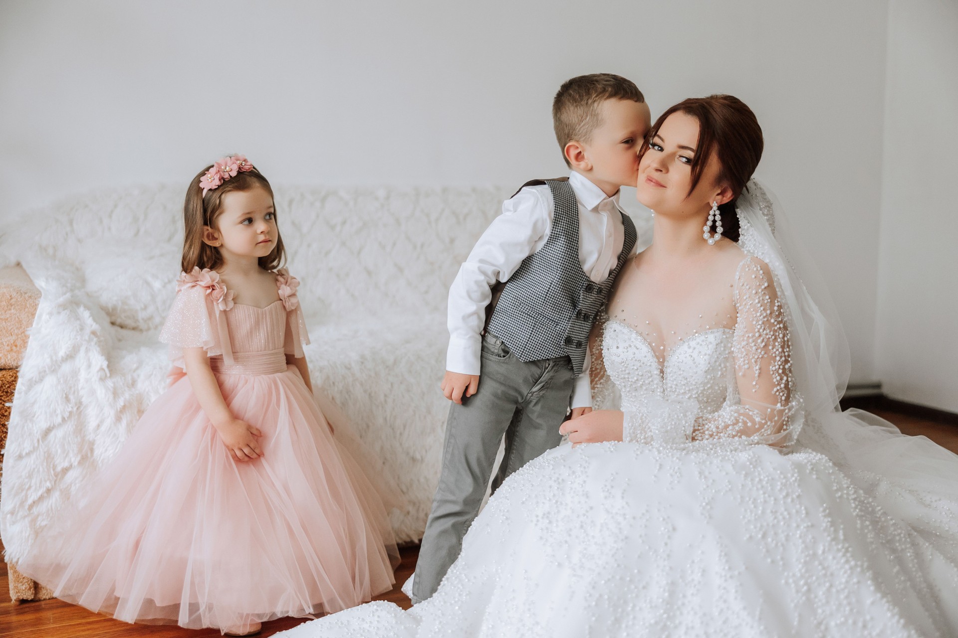 The bride is photographed with small children on the wedding day. A little boy kisses his bride on the cheek.